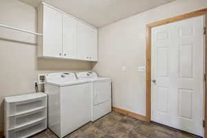 Washroom with cabinet space, dark stone finish flooring, washing machine and clothes dryer, and a textured ceiling