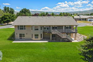 Rear view of property featuring a patio, a deck with mountain view, stucco siding, stairs, and a lawn