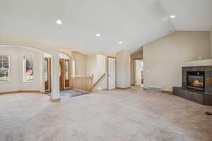 Unfurnished living room featuring carpet floors, vaulted ceiling, recessed lighting, and a tiled fireplace
