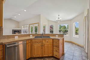 Kitchen featuring stainless steel dishwasher, tile counters, a chandelier, a tiled fireplace, and pendant lighting