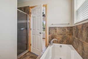 Full bath with a garden tub, a shower stall, and stone finish flooring
