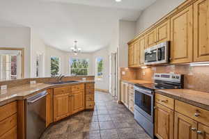 Kitchen featuring stainless steel appliances, backsplash, a chandelier, tile countertops, and dark stone finish flooring
