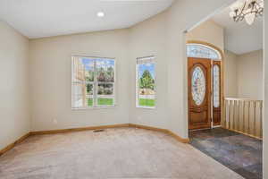 Entryway with plenty of natural light, a chandelier, carpet, and high vaulted ceiling