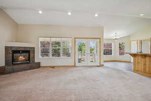 Unfurnished living room with carpet flooring, a chandelier, a fireplace, french doors, and recessed lighting