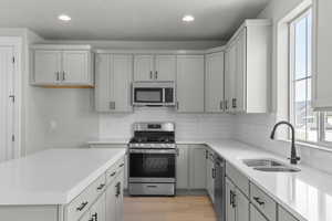 Kitchen with appliances with stainless steel finishes, a textured ceiling, a center island, decorative backsplash, and light wood-style floors