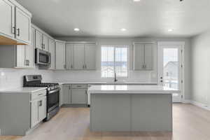 Kitchen featuring stainless steel appliances, a textured ceiling, gray cabinets, light wood-style floors, and a kitchen island