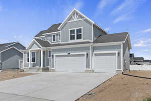 View of front facade with board and batten siding, roof with shingles, driveway, and a garage