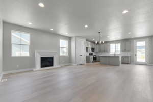 Unfurnished living room featuring a textured ceiling, light wood-style flooring, a glass covered fireplace, a chandelier, and recessed lighting