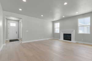 Unfurnished living room featuring recessed lighting, light wood-type flooring, a glass covered fireplace, and a textured ceiling