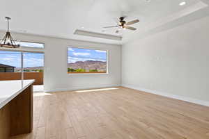 Unfurnished living room featuring a tray ceiling, light wood-type flooring, a chandelier, ceiling fan, and recessed lighting