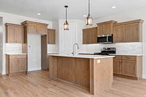 Kitchen with appliances with stainless steel finishes, light wood-style floors, backsplash, brown cabinetry, and recessed lighting
