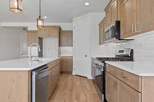 Kitchen with appliances with stainless steel finishes, light wood-type flooring, tasteful backsplash, recessed lighting, and light countertops