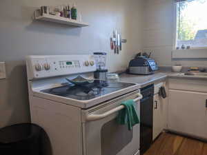 Kitchen with white range with electric cooktop, white cabinetry, dark wood-style flooring, black dishwasher, and light countertops