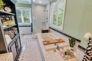 Bathroom with light tile patterned floors, a jetted tub, tile walls, a shower stall, and plenty of natural light