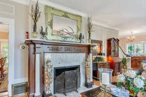 Detailed view of crown molding, a fireplace, a chandelier, and wood finished floors