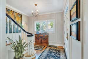 Foyer entrance with wood-type flooring, a decorative wall, ornamental molding, arched walkways, and a chandelier