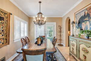 Dining area with arched walkways, ornamental molding, a chandelier, and light tile patterned floors