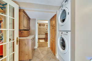 Laundry room featuring light tile patterned flooring, cabinet space, stacked washing machine and dryer, and a textured ceiling