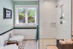 Full bath featuring a shower stall, tile patterned floors, tile walls, a bidet, and a wainscoted wall