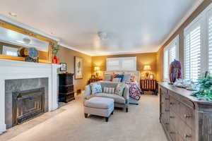 Bedroom with light colored carpet, ornamental molding, and a fireplace