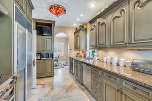 Kitchen with recessed lighting, built in appliances, light stone counters, and arched walkways