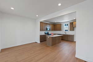 Kitchen featuring light wood-type flooring, light countertops, recessed lighting, electric range, and a kitchen island