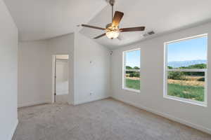 Spare room featuring a ceiling fan, light colored carpet, vaulted ceiling, and a mountain view