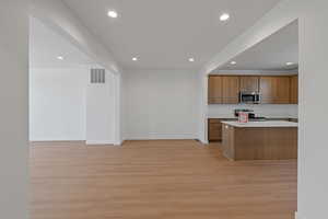 Kitchen with recessed lighting, light wood-type flooring, light countertops, stainless steel appliances, and brown cabinetry