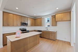 Kitchen with appliances with stainless steel finishes, light wood-style flooring, a center island, light countertops, and brown cabinets