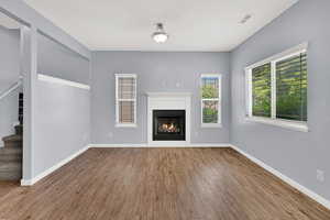 Unfurnished living room featuring stairway, wood finished floors, and a warm lit fireplace