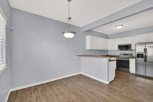 Kitchen with stainless steel appliances, white cabinetry, dark wood-style flooring, and a peninsula