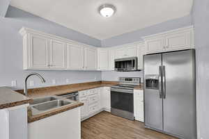 Kitchen with appliances with stainless steel finishes, a peninsula, light wood-style floors, white cabinetry, and dark countertops