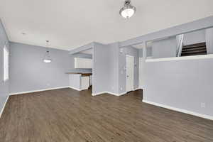 Unfurnished living room featuring dark wood-style floors and stairs