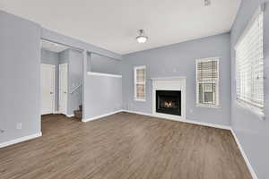 Unfurnished living room with wood finished floors, a lit fireplace, and stairway