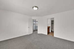 Unfurnished bedroom with dark carpet, a textured ceiling, and ensuite bathroom