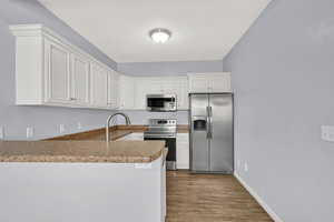 Kitchen with appliances with stainless steel finishes, a peninsula, dark wood-type flooring, and white cabinets