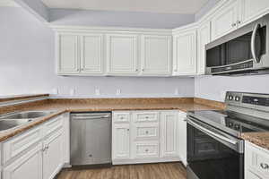 Kitchen with appliances with stainless steel finishes, white cabinetry, and wood finished floors