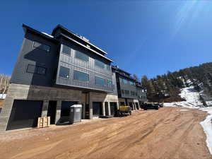 Snow covered property with stone siding, dirt driveway, and a garage