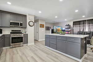 Kitchen featuring appliances with stainless steel finishes, gray cabinetry, light countertops, light wood-type flooring, and recessed lighting
