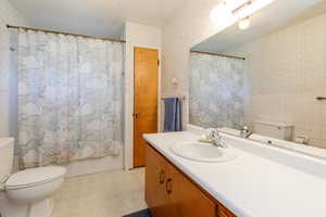 Bathroom with wallpapered walls, a wainscoted wall, vanity, tile patterned floors, and shower / tub combo