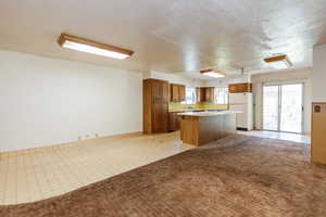 Kitchen with freestanding refrigerator, a center island, brown cabinets, light countertops, and light carpet
