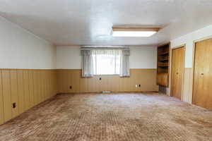 Carpeted spare room with a wainscoted wall and wood walls