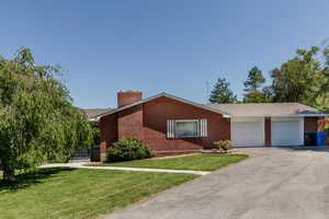 View of front of property with brick siding, a chimney, an attached garage, a front lawn, and asphalt driveway