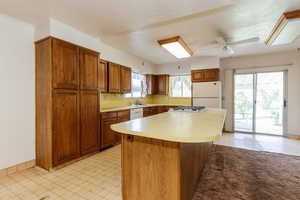 Kitchen with white appliances, brown cabinetry, light countertops, and a center island