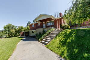 View of front of home featuring asphalt driveway, a chimney, covered porch, brick siding, and stairs