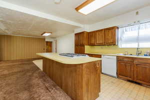 Kitchen with dishwasher, gas cooktop, light countertops, a kitchen island, and brown cabinets