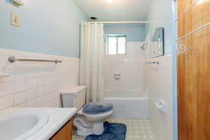 Full bathroom with tile walls, tile patterned floors, vanity, shower / tub combo with curtain, and a wainscoted wall