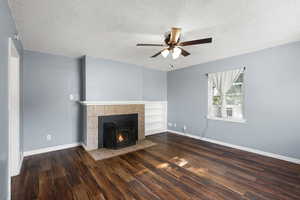Unfurnished living room with ceiling fan, wood finished floors, a textured ceiling, a fireplace, and cooling unit