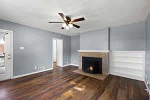 Unfurnished living room featuring a ceiling fan, wood finished floors, a textured ceiling, and a tiled fireplace