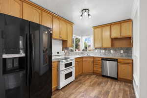Kitchen featuring black fridge with ice dispenser, stainless steel dishwasher, double oven range, decorative backsplash, and dark wood-style floors